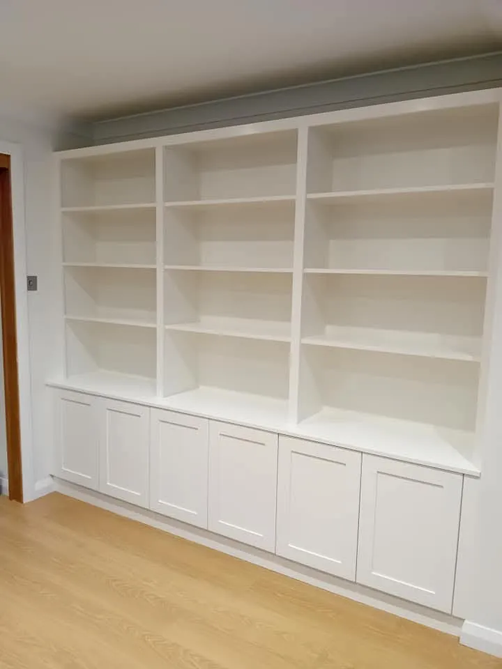 A room with white bookcases and wooden floors.