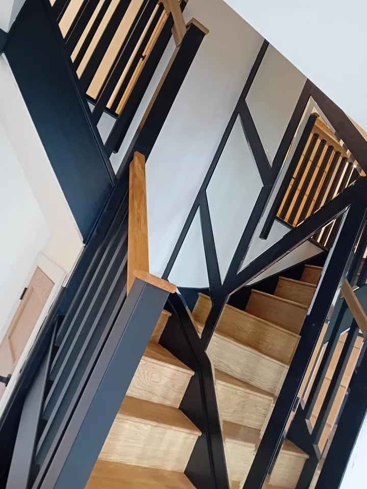 A wooden staircase with black railing and handrails.